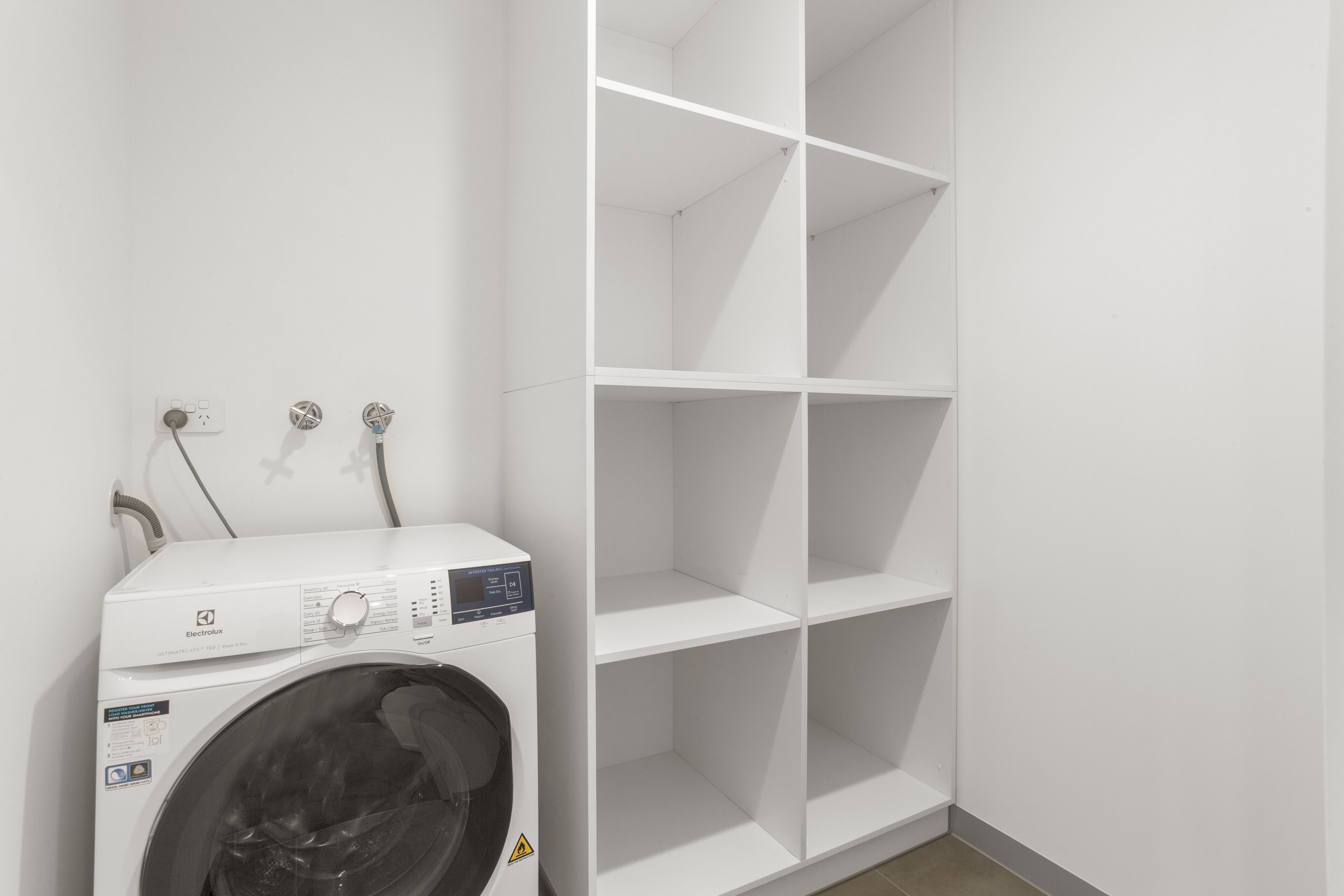Un área de lavandería con una lavadora blanca y un estante blanco.
