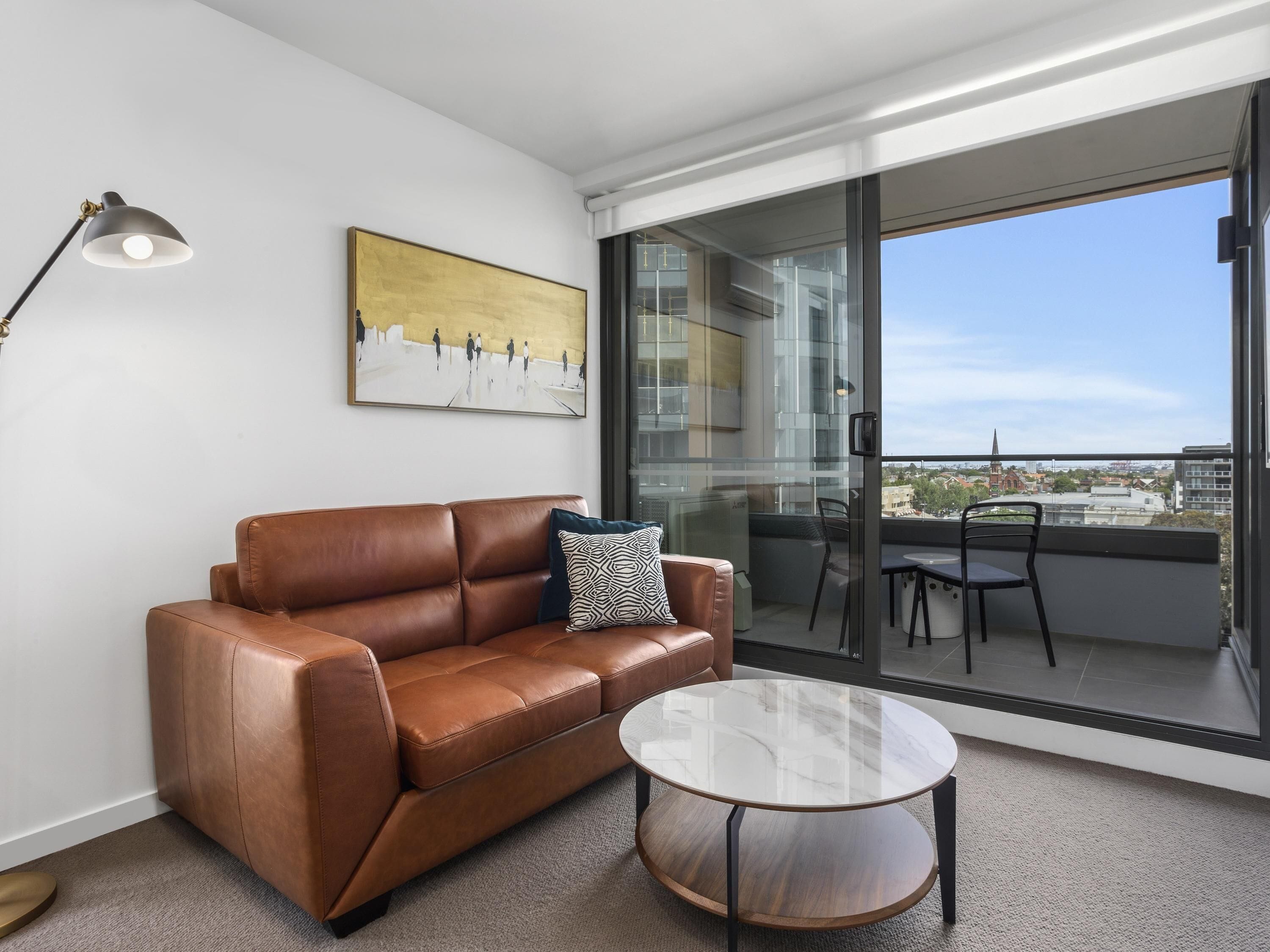 Un salón moderno con un sofá de cuero marrón, una mesa de centro de vidrio y un cuadro en la pared.