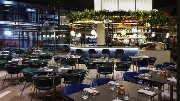 Un restaurant doté de nombreuses tables et chaises, d’un bar et offrant une vue sur le paysage urbain.