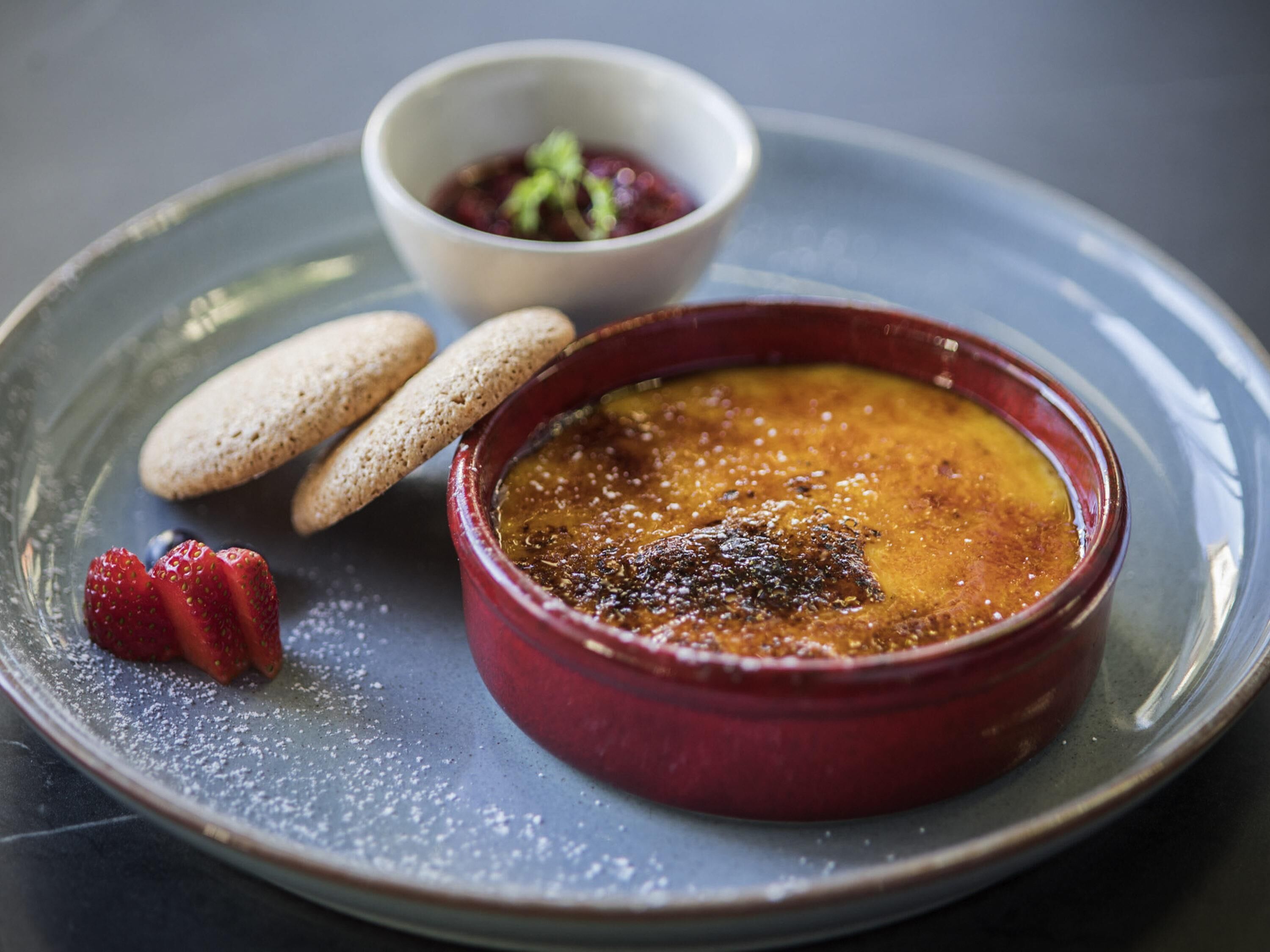 Un piattino con crema bruciata, fragole e biscotti.