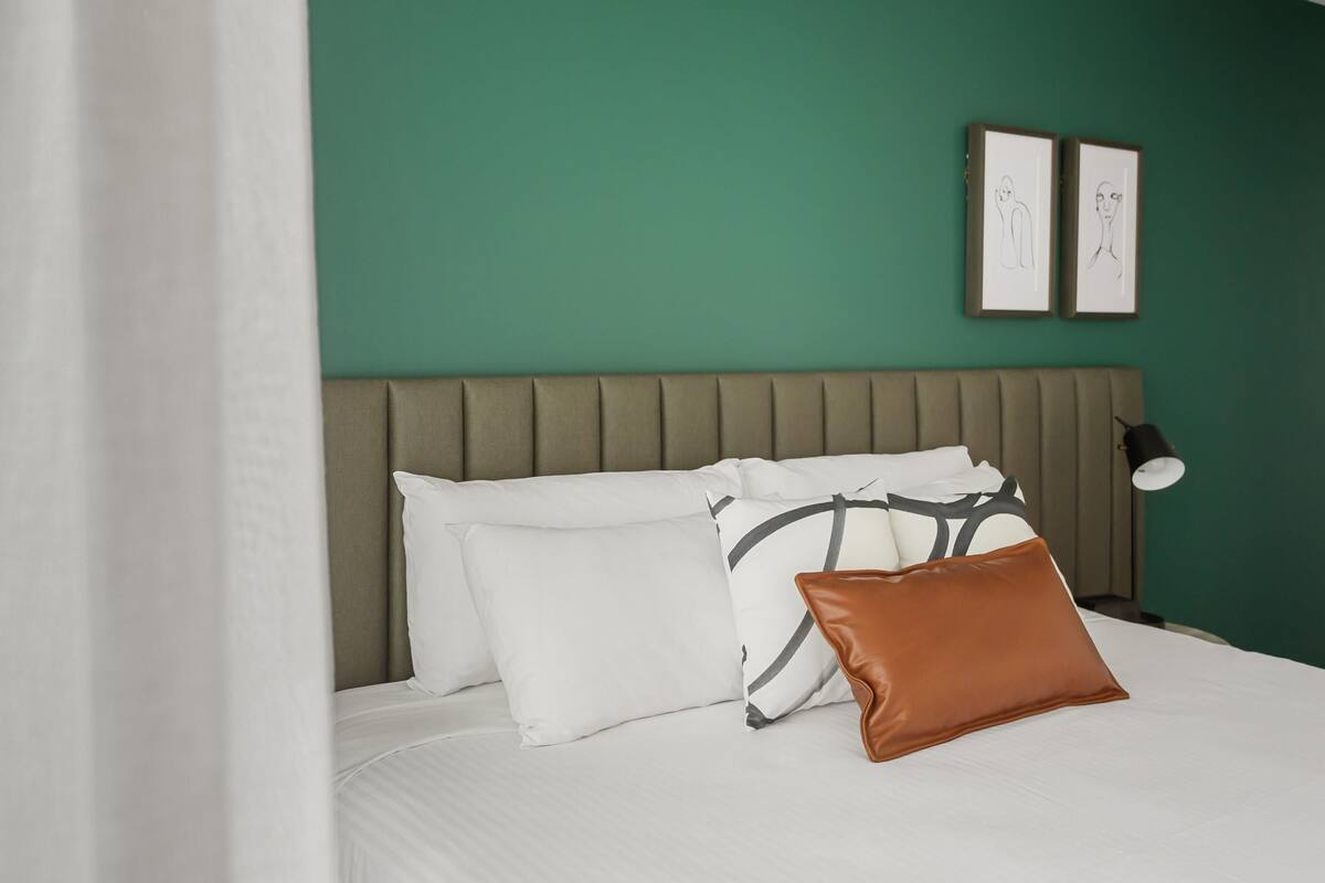 A bed with white bedding, a brown pillow, and a headboard against a green wall.