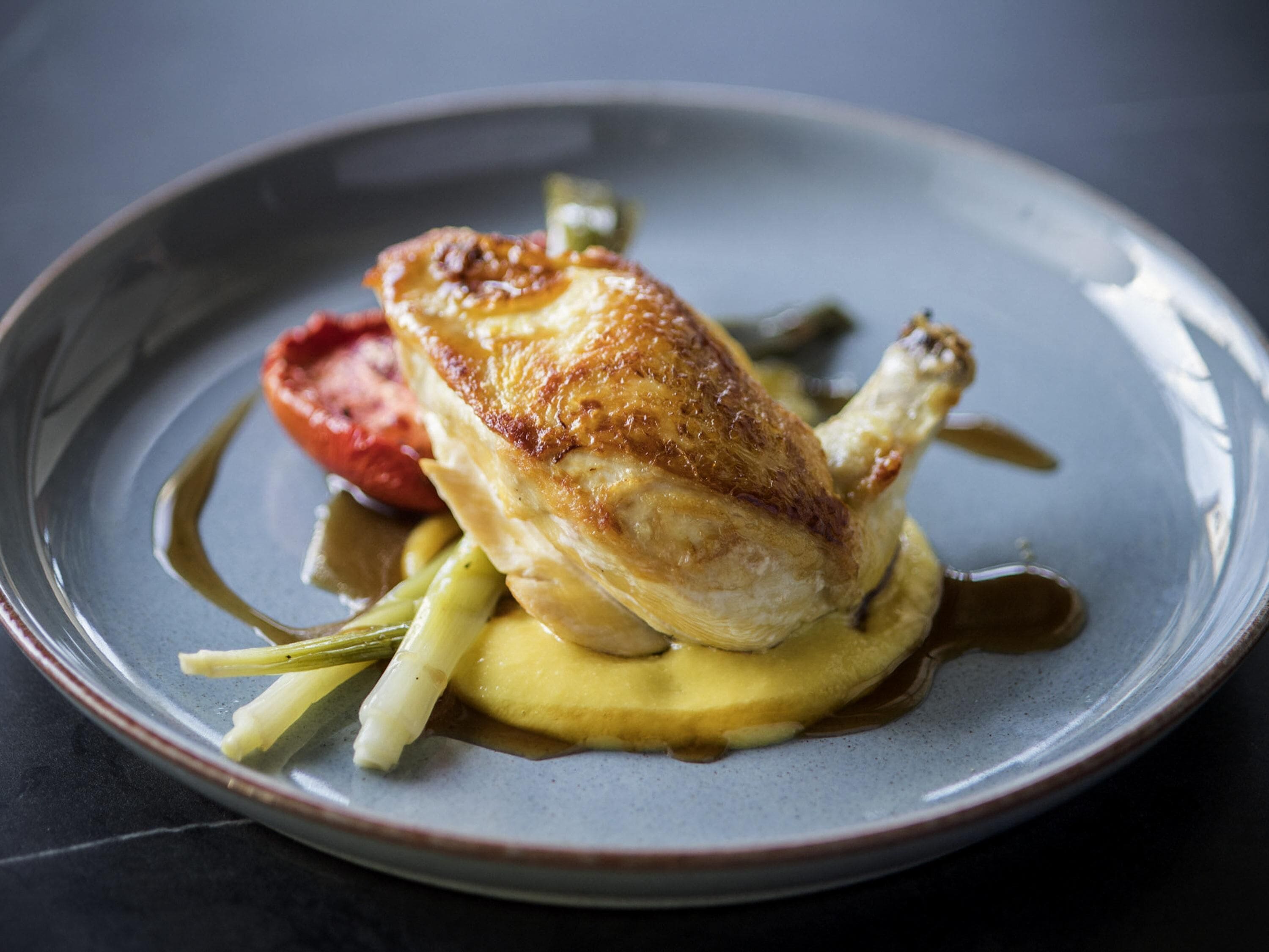 A plate with a roasted chicken, vegetables, and sauce.
