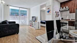 Un apartamento moderno con sala de estar, comedor, kitchenette y balcón con vista a una obra en construcción.