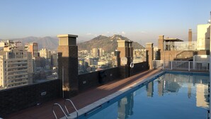 Piscina en la azotea con vistas a la ciudad, pilares de ladrillo y una terraza de madera.