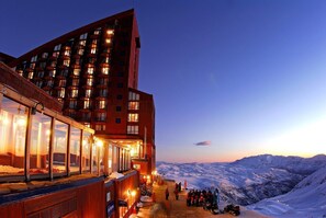Un hotel con varios pisos, amplias ventanas y vistas a una cadena montañosa nevada.