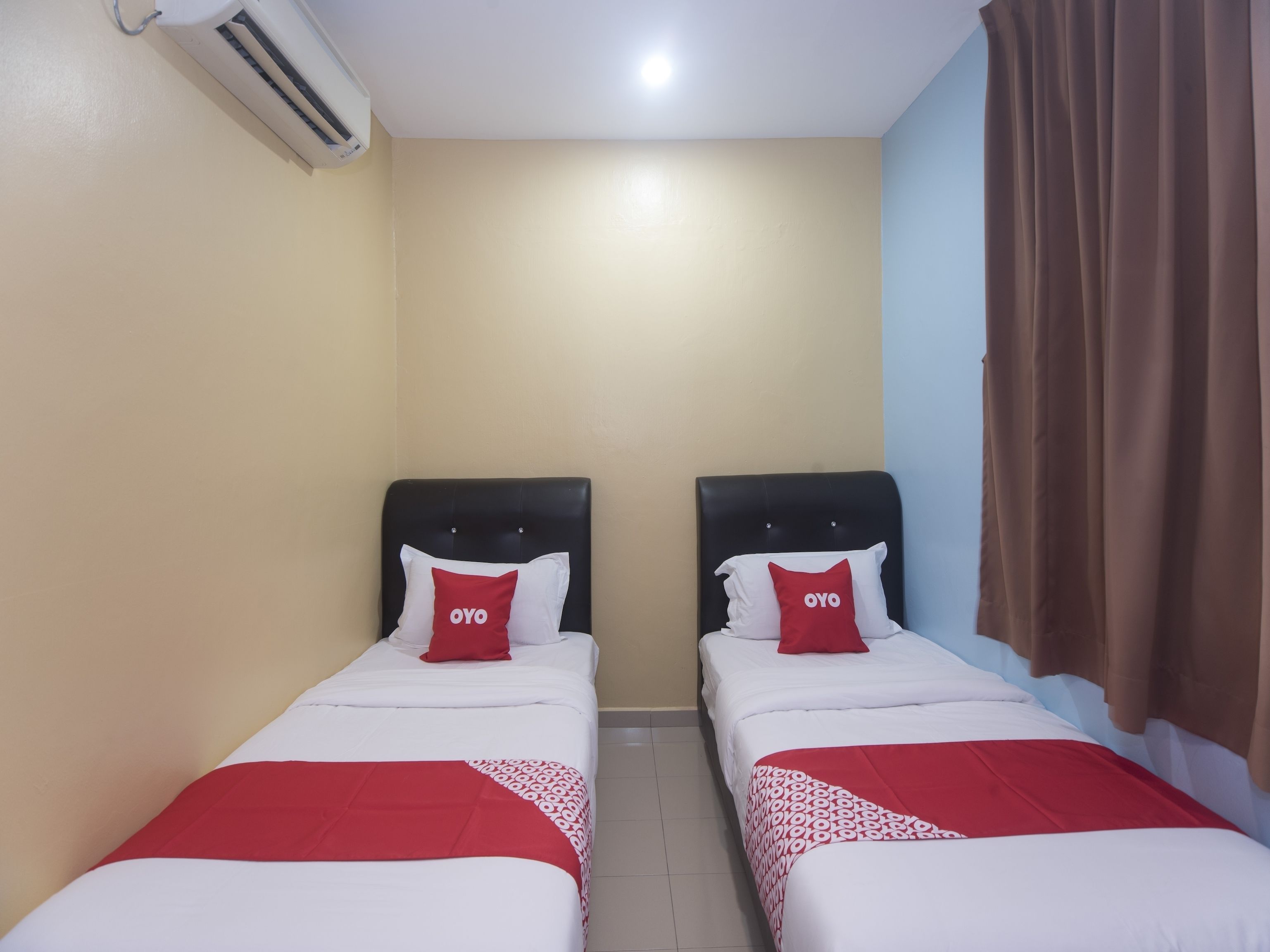 A hotel room with two single beds, each with a red and white pillow, a red blanket, and a black headboard.