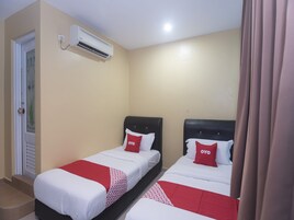 A hotel room with two beds, each with a red and white bedspread and matching pillows. An air conditioning unit is mounted on the wall above the beds.