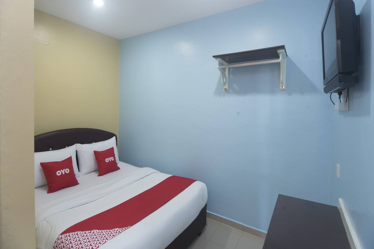 A hotel room with a bed, a TV mounted on the wall, and a small shelf above the bed.