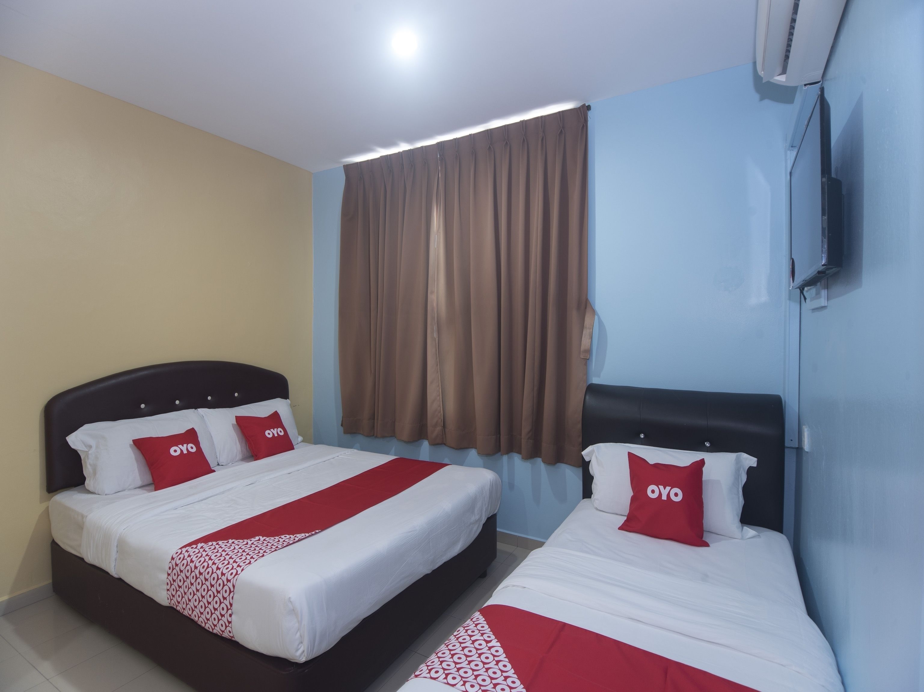 A hotel room with two beds, each with a headboard, a large window with curtains, and a wall-mounted TV.