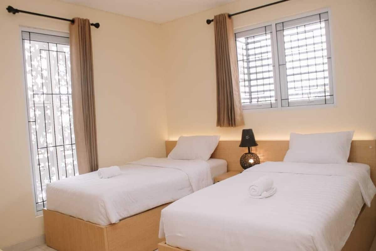 Una habitación de hotel con dos camas individuales, una mesita de noche con lámpara y una ventana con cortinas.