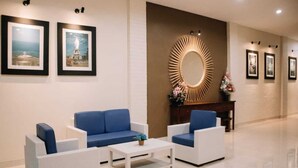Eine Hotellobby mit einer Rezeption, blauen Sofas, einem weißen Couchtisch, gerahmten Bildern an der Wand und einem dekorativen Spiegel.