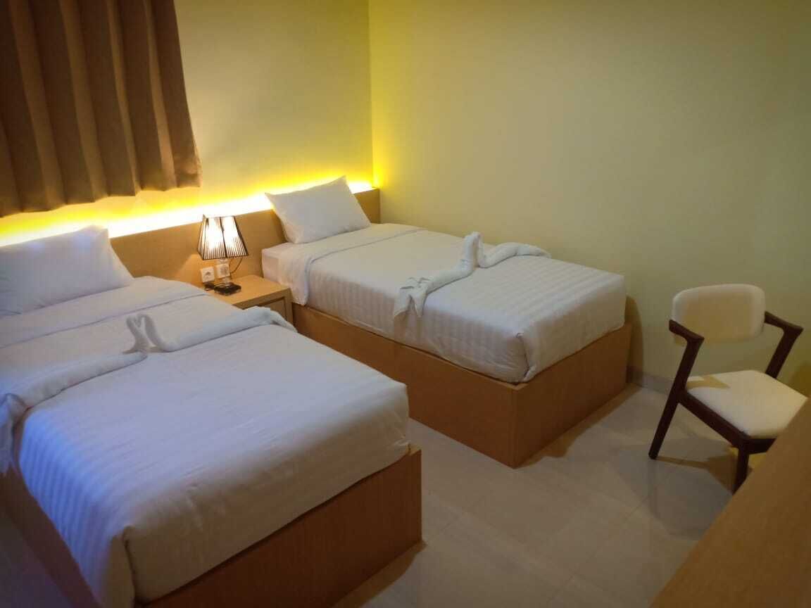 Habitación de hotel con dos camas, una mesita de noche, una silla y una lámpara.