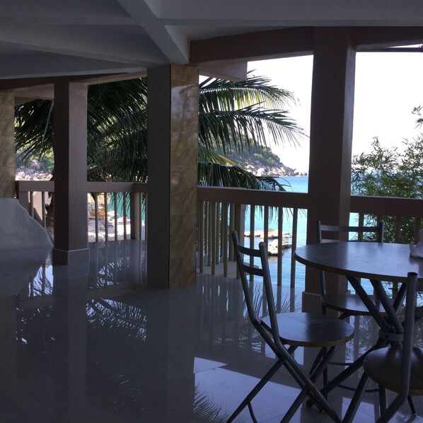 A dining area with a view of the sea, featuring a table and chairs, and a balcony with palm trees. - Hinwong Apartments Dive & Snorkel Resort (Koh Tao)
