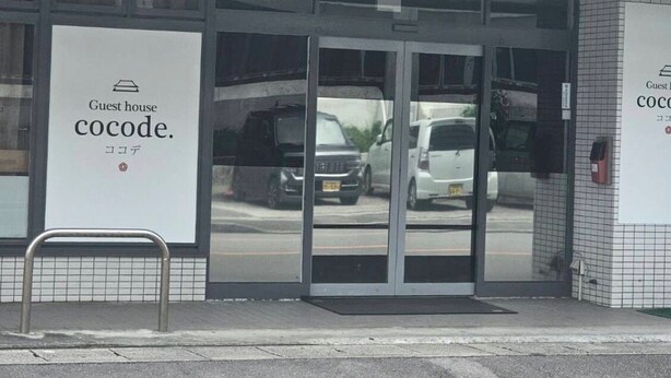 L’entrée d’une maison d’hôtes, avec une porte en verre et une enseigne indiquant : « Maison d’hôtes Cocode ».