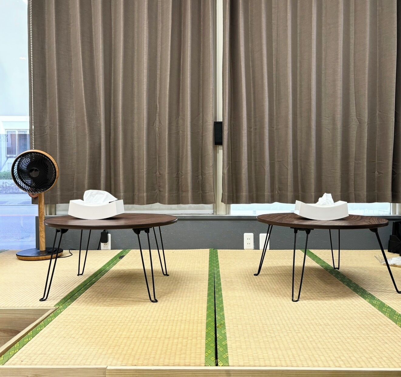Una habitación con dos mesas, un ventilador y una ventana con cortinas.