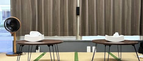 Una habitación con dos mesas, un ventilador y una ventana con cortinas.
