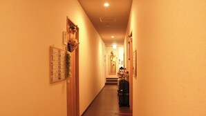 Un couloir étroit avec une porte en bois sur la gauche, un calendrier accroché au mur et un escalier menant à l’étage supérieur.