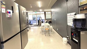 Un hall d’hôtel comprenant un comptoir d’accueil, un espace repas, une machine à café et un calendrier mural.