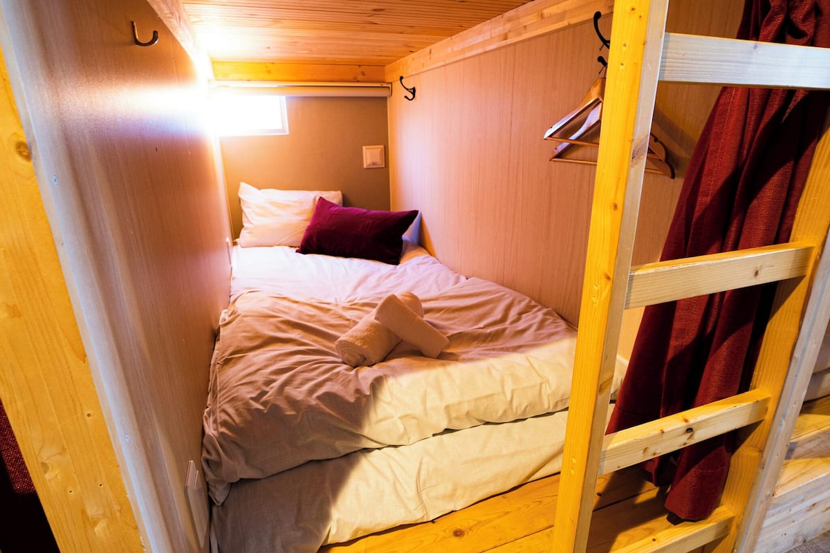 A small, cozy room with a bunk bed, a single bed, and a wooden ladder.