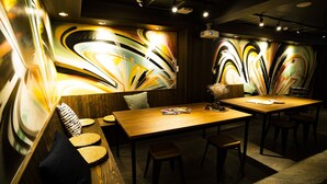 A modern restaurant with a wooden table and chairs, a bench with cushions, and abstract wall art. - R Hostel Namba South (Osaka)
