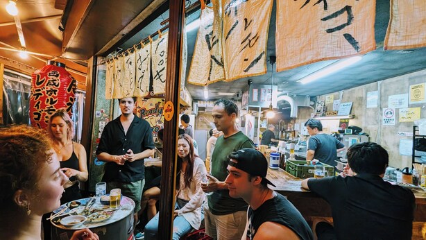 A busy restaurant interior with tables, chairs, and hanging decorations. - R Hostel Namba South (Osaka)
