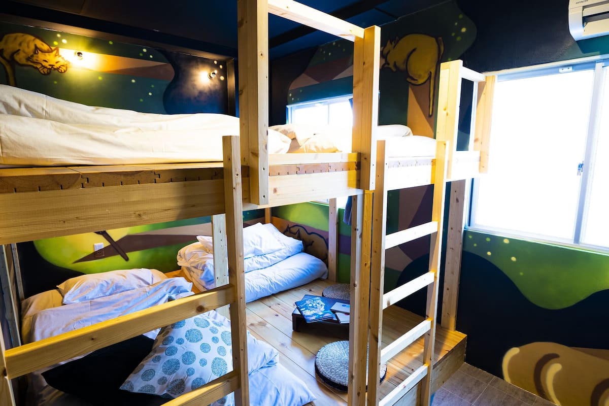 A bunk bed room with a mural on the wall, a window, and a small table with books.