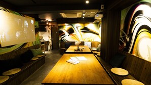 A restaurant with a long wooden table, cushioned seating, and a colorful abstract mural on the wall. - R Hostel Namba South (Osaka)
