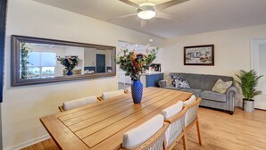 A dining area with a wooden table, chairs, a vase of flowers, a ceiling fan, a sofa, and a framed picture on the wall. - Gorgeous Downtown Delray Beach Cottage (Delray Beach)