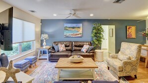 A living room with a brown leather sofa, a patterned armchair, a coffee table, and a painting of a coastal scene. - Gorgeous Downtown Delray Beach Cottage (Delray Beach)