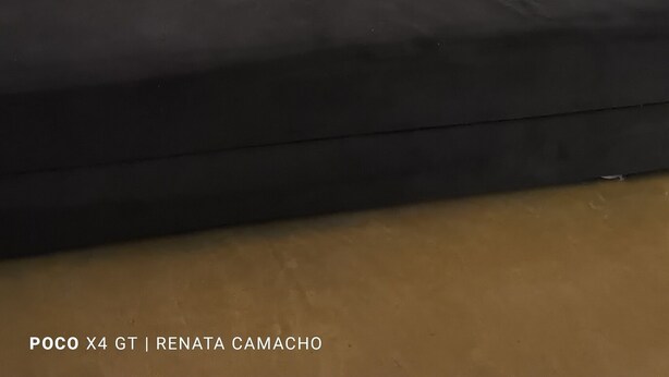 Ein Wohnzimmer mit einer schwarzen Couch und drei farbenfrohen Wandbildern, die städtische Szenen zeigen.