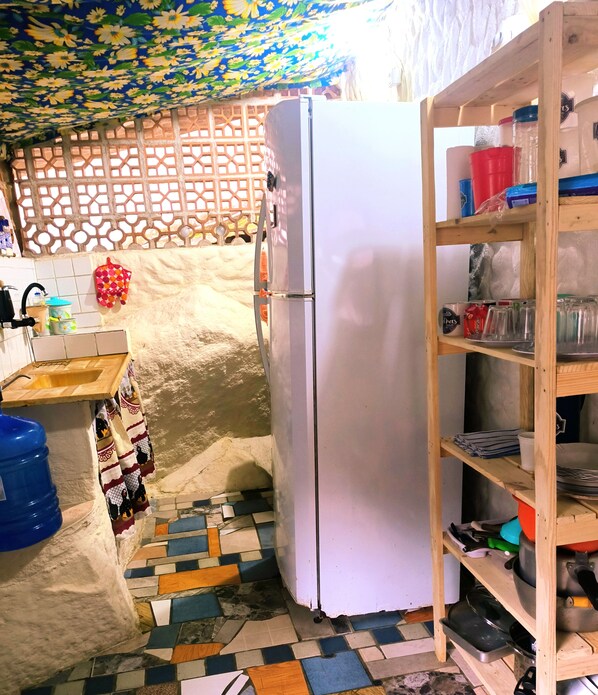 Una cocina con refrigerador, pileta y una estantería de madera con utensilios de cocina.
