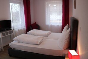 Una habitación de hotel con dos camas, un escritorio con televisor de pantalla plana y una lámpara de noche.