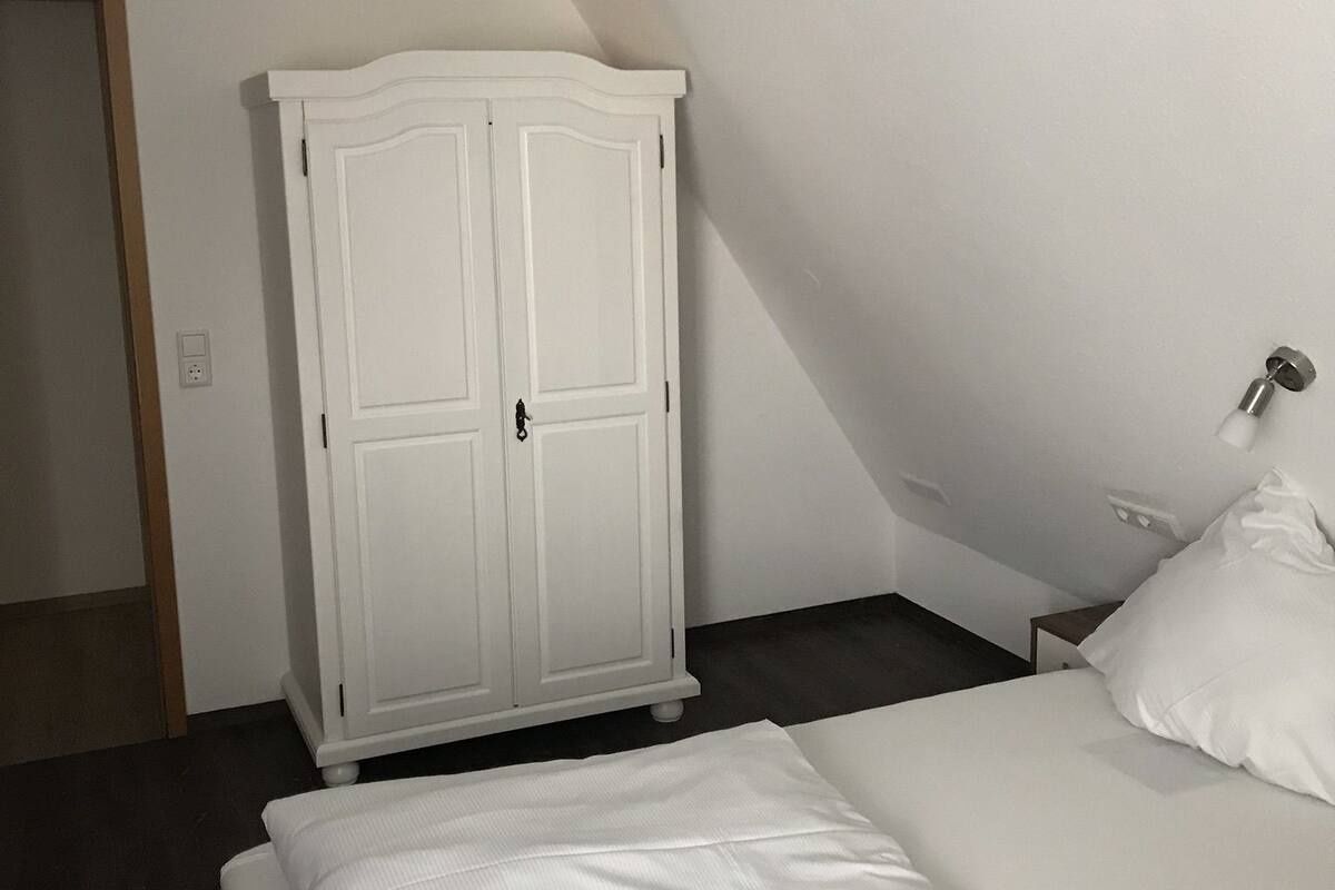 A bedroom with a bed, a white wardrobe, and a door.