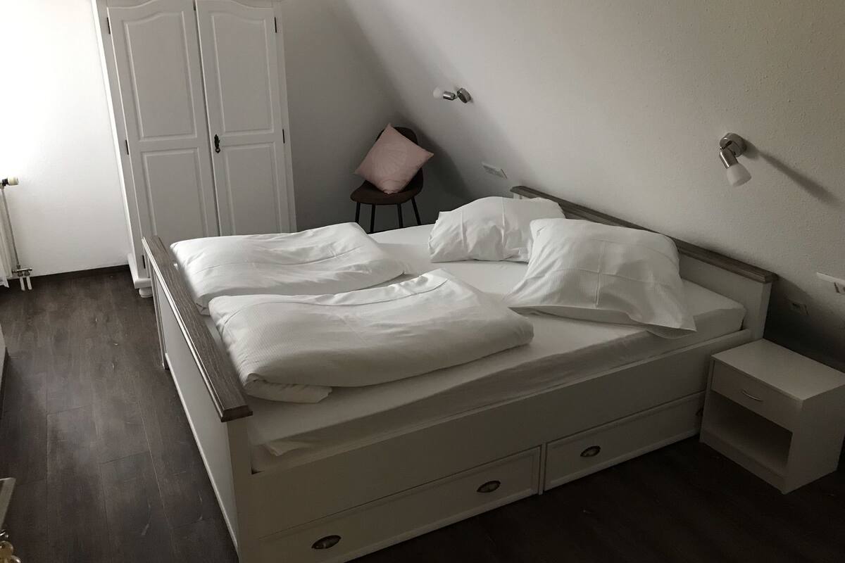 A bedroom with a bed, a nightstand, a chair, and a wardrobe.