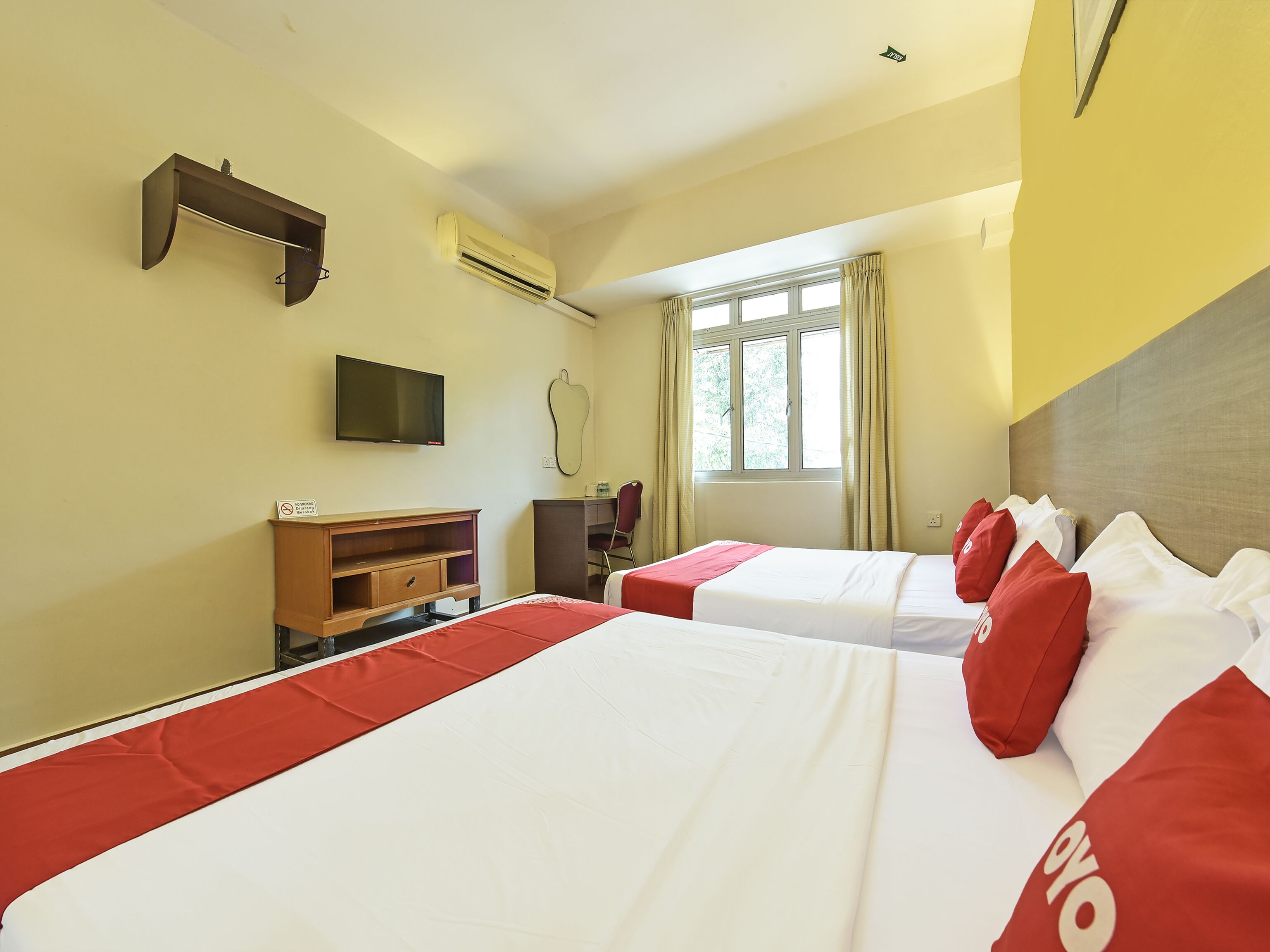 A hotel room with two beds, a TV, a desk, and a window with curtains.