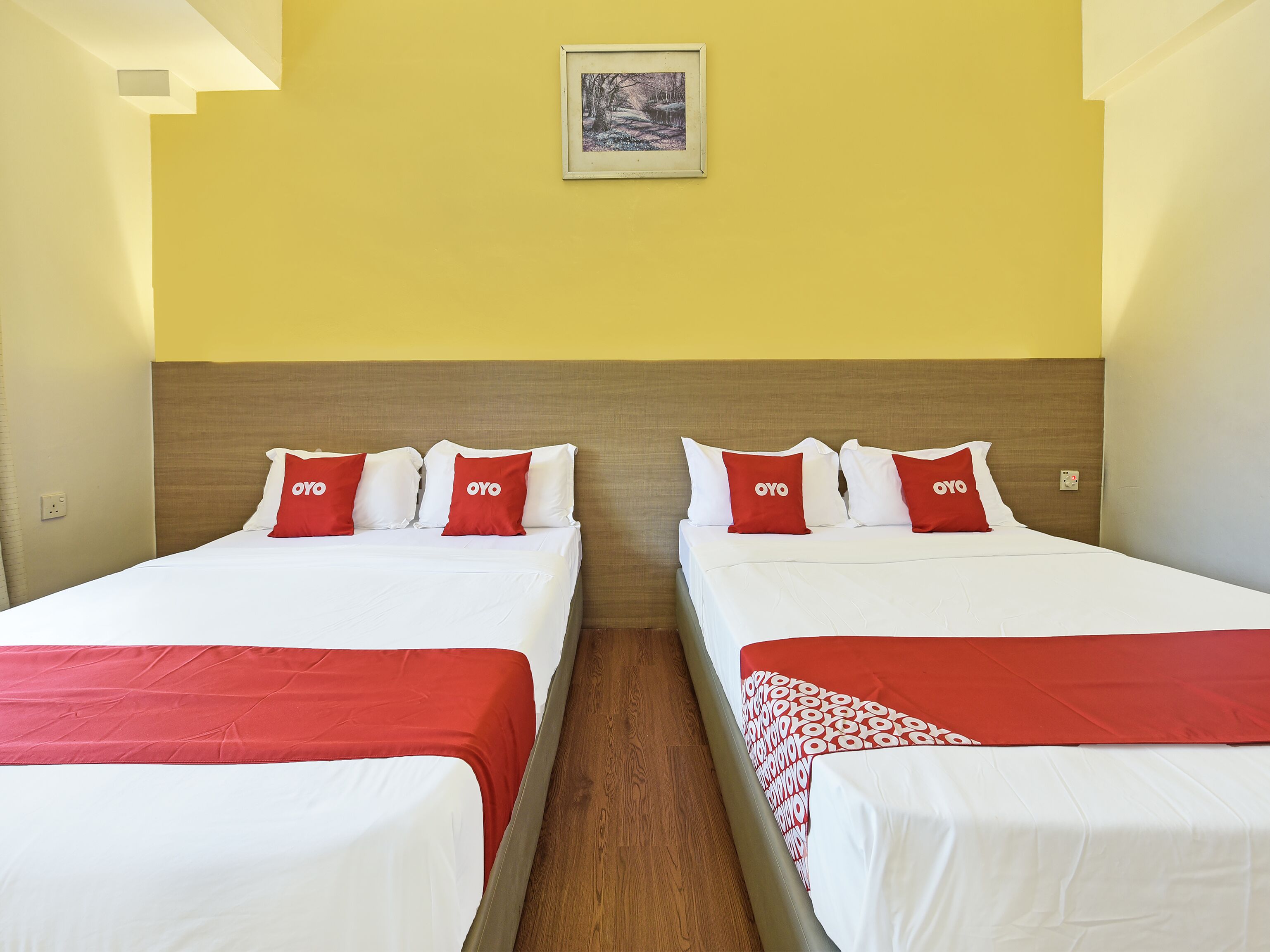 Een hotelkamer met twee bedden, elk met witte lakens en rode kussens, en een ingelijst kunstwerk aan de muur.