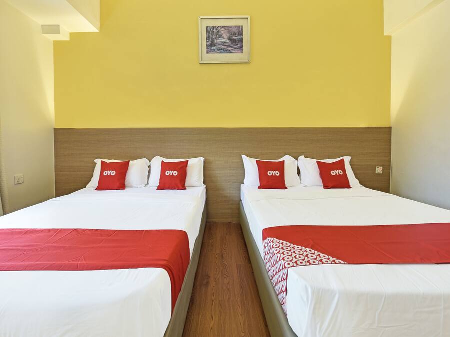 Een hotelkamer met twee bedden, elk met witte lakens en rode kussens, en een ingelijst kunstwerk aan de muur.