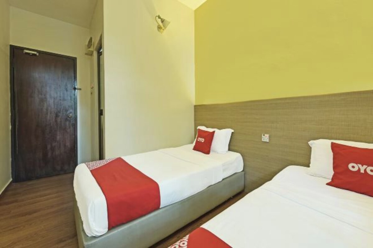 A hotel room with two beds, each with white bedding and red accents, a wooden headboard, and a door in the background.