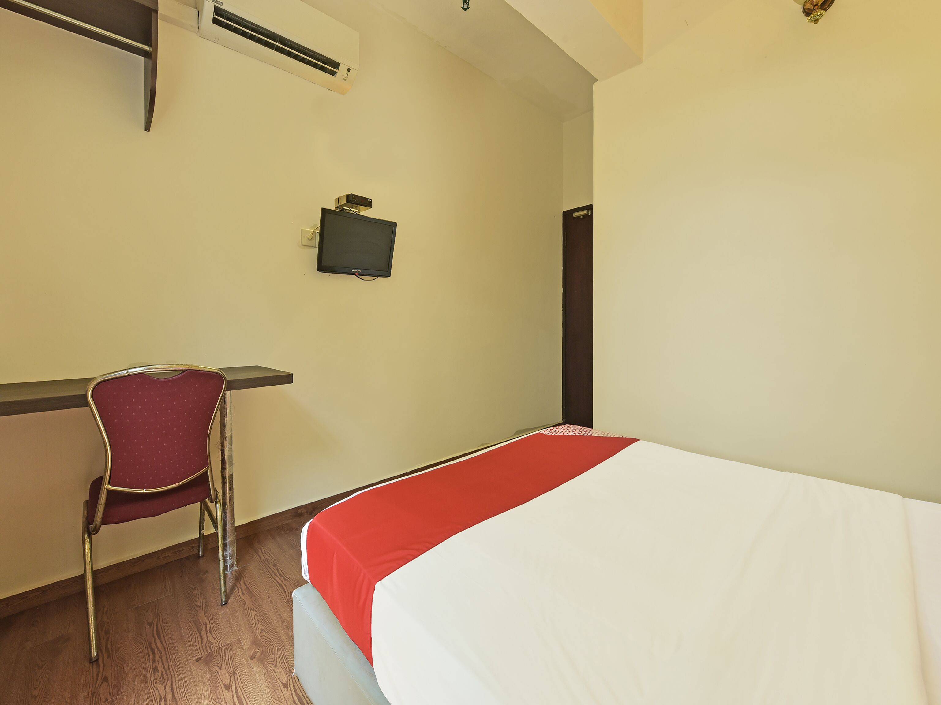 A hotel room with a bed, a desk, a chair, an air conditioner, and a television.