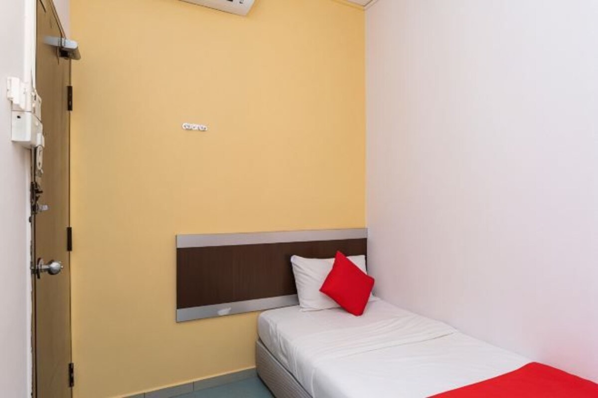 A single bed with a wooden headboard, a red pillow, and a white blanket.