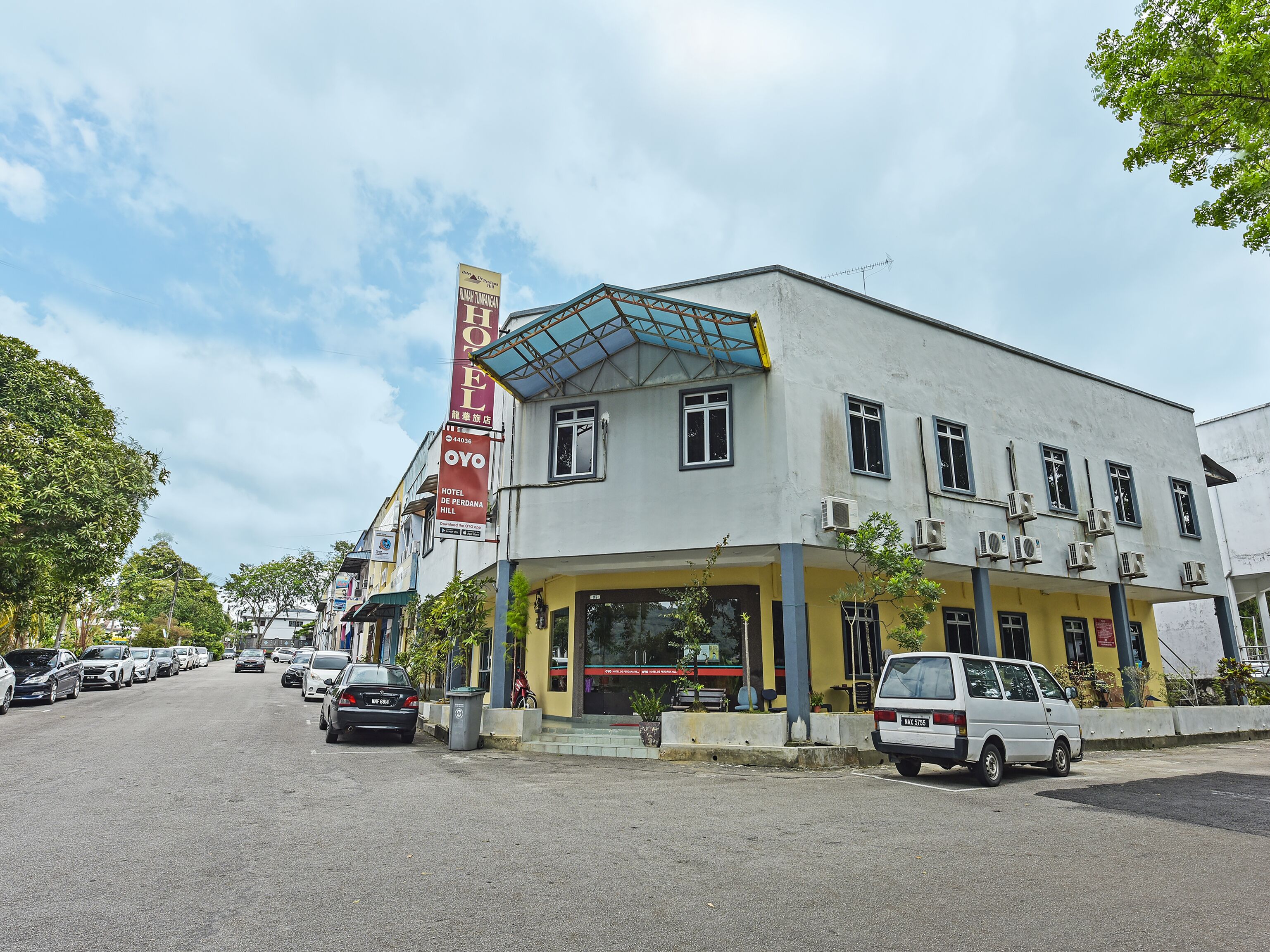 A hotel with a large sign, multiple air conditioning units, and parked cars on the street.