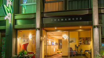 Entrada de un hotel con un letrero de neón, un mostrador de recepción y una zona de estar visible a través de puertas de cristal.