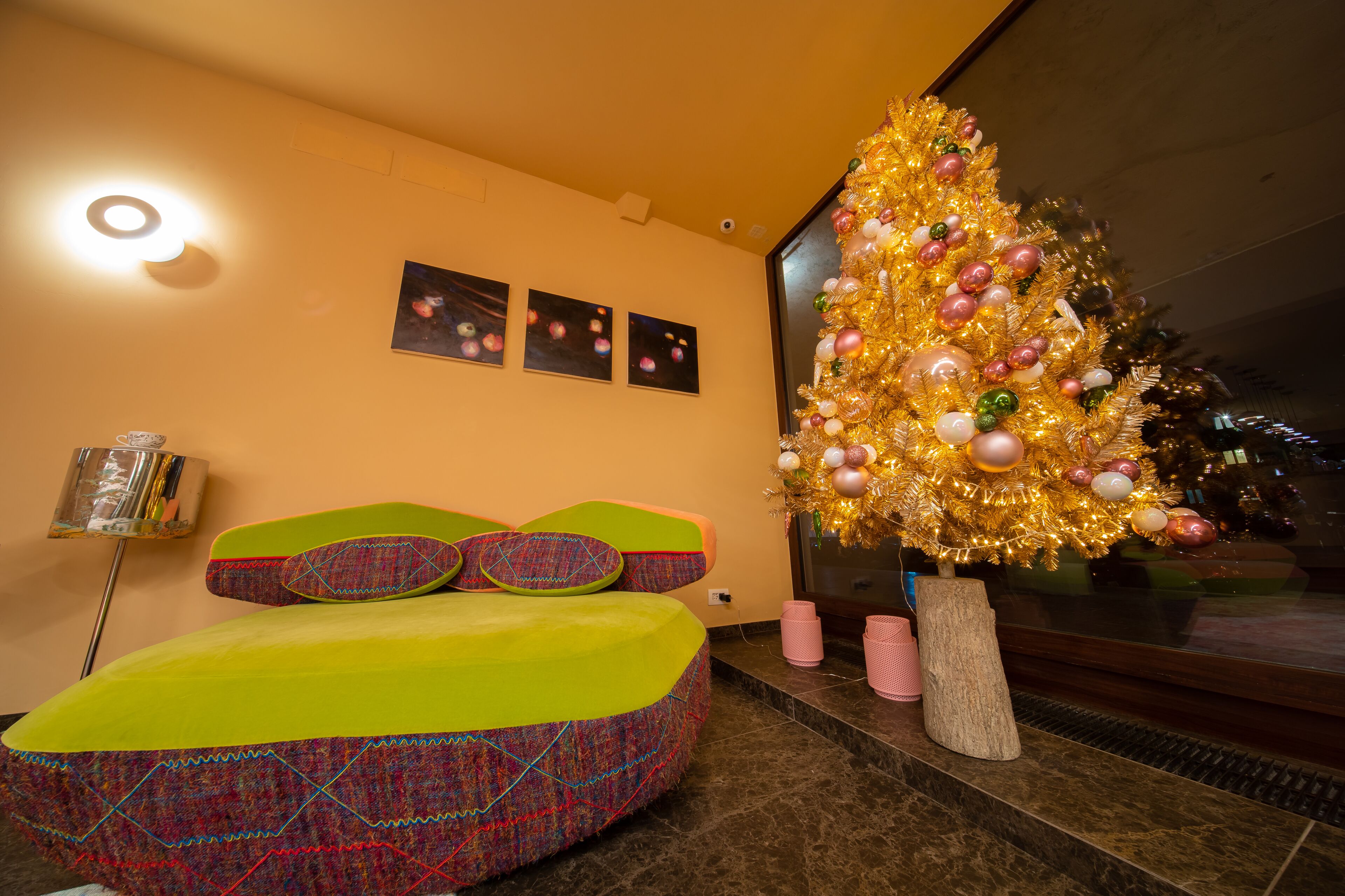 Una habitación moderna con una cama colorida, un abeto navideño grande y tres cuadros en la pared.