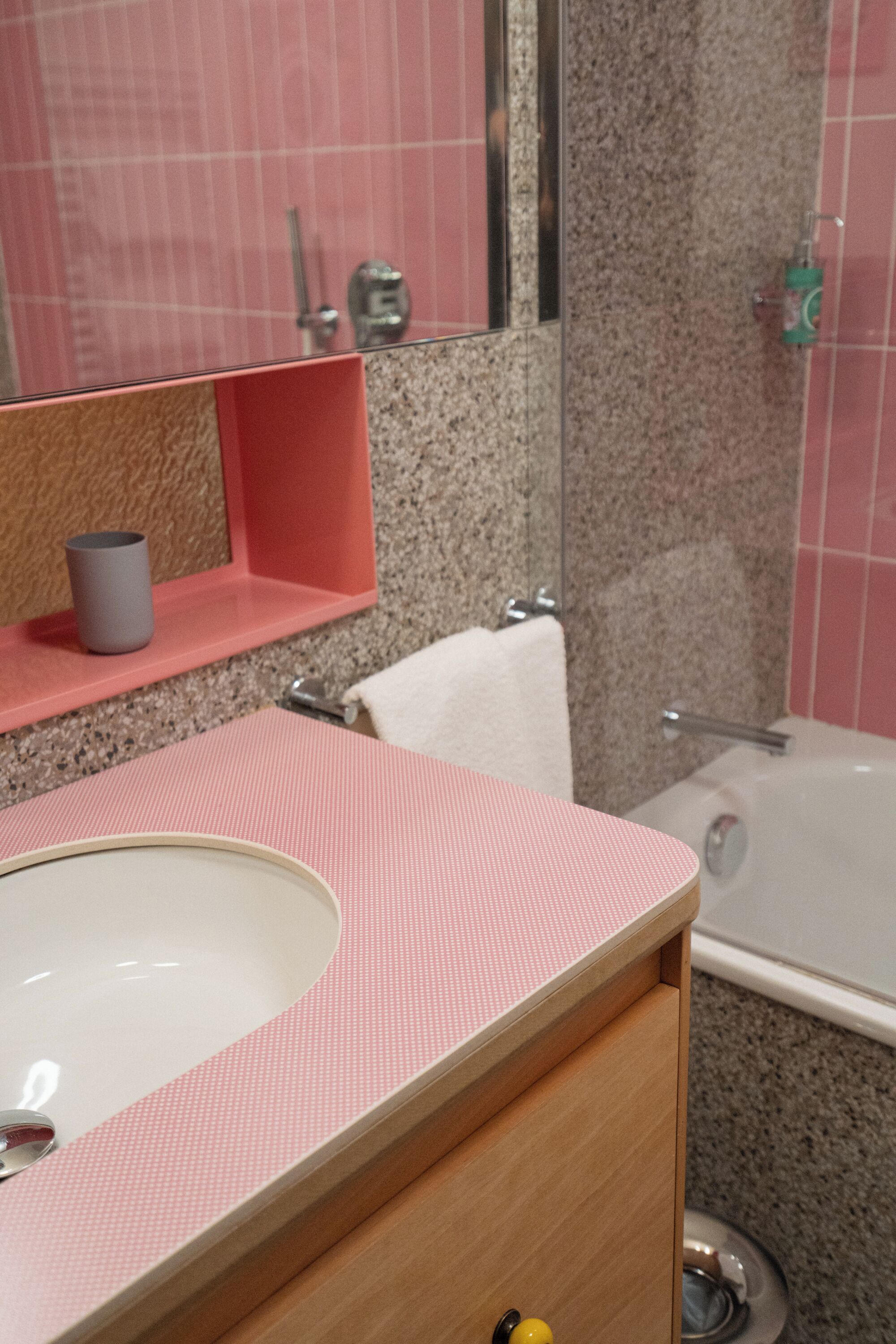 Un baño con un lavamanos rosa, un espejo, un perchero para toallas y una bañera.