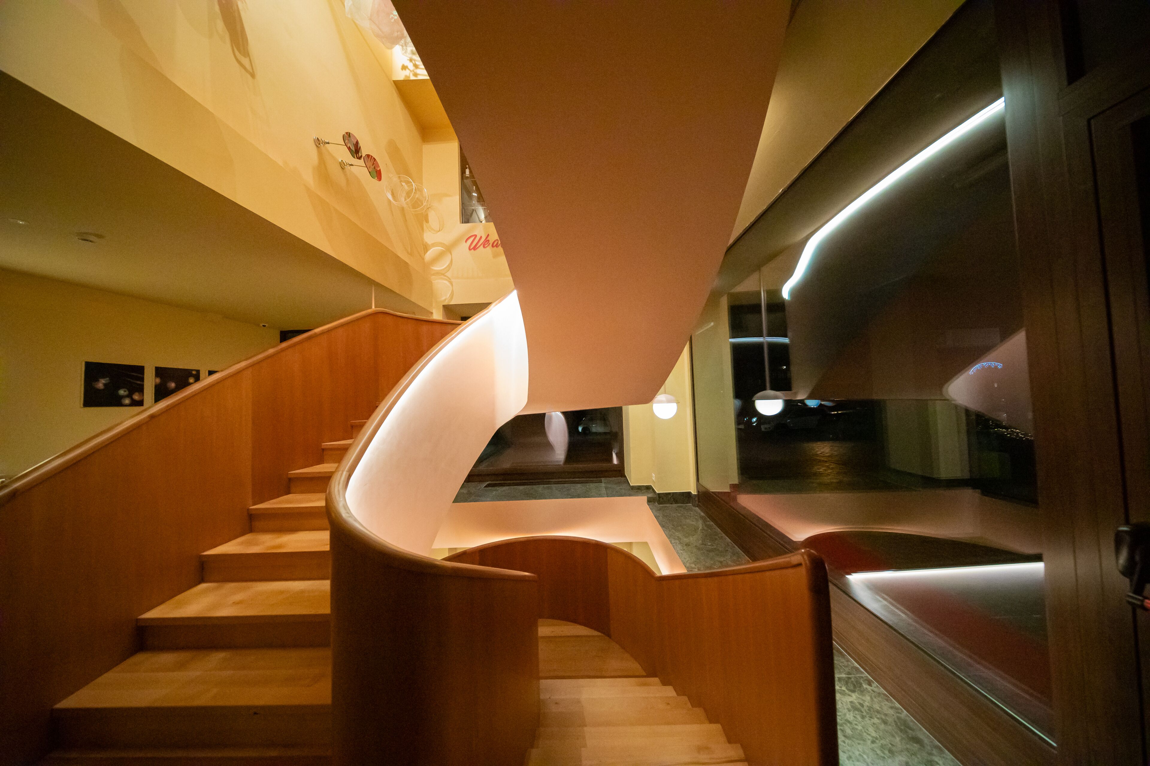 A spiral staircase with wooden steps and a curved handrail, leading to a landing with a glass partition.