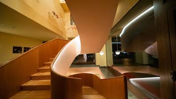 Una escalera de caracol con escalones de madera y una barandilla curva, que lleva a un rellano con una partición de vidrio.