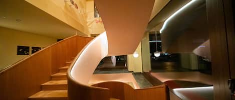 A spiral staircase with wooden steps and a curved handrail, leading to a landing with a glass partition.
