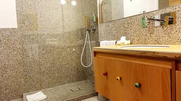 Een moderne badkamer met een douche van graniet, een houten wastafelmeubel en een grote spiegel.