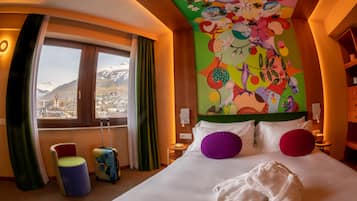 Una habitación de hotel con una cama, arte murales coloridos y vistas a montañas, además de una ventana con cortinas.