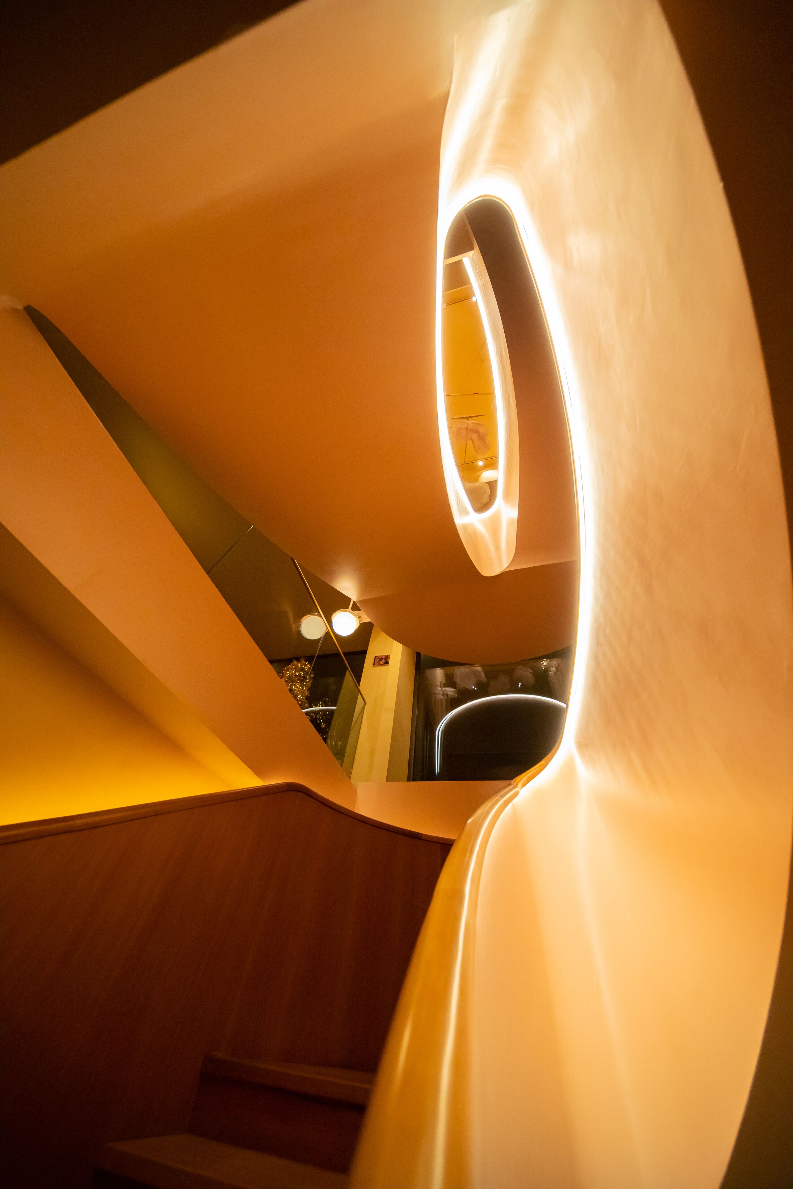 A spiral staircase with a circular light fixture at the top, wooden steps, and a modern interior design.